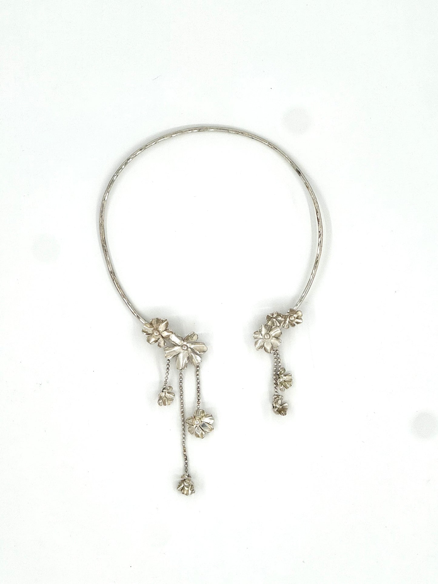 A silver-toned open cuff bracelet with dangling floral and chain embellishments, photographed on a plain white background.
