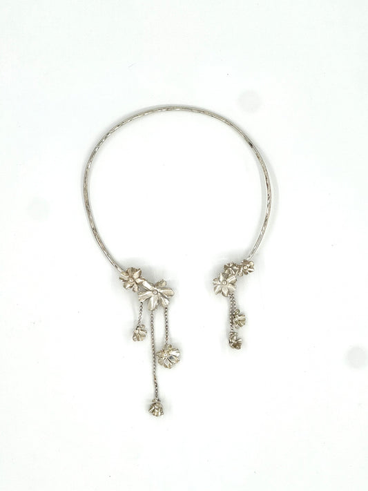 A silver-toned open cuff bracelet with dangling floral and chain embellishments, photographed on a plain white background.