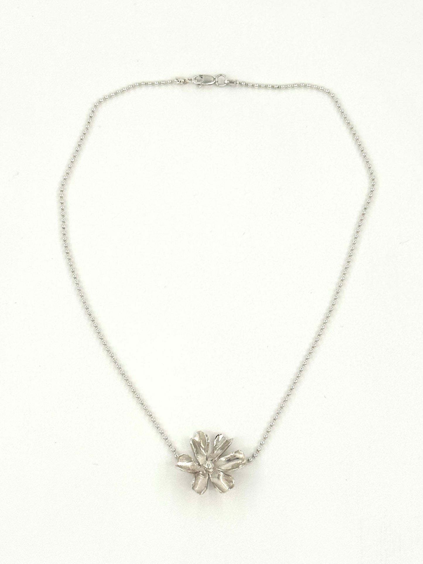 A silver chain necklace with a textured, flower-like metallic pendant, displayed against a plain white background.
