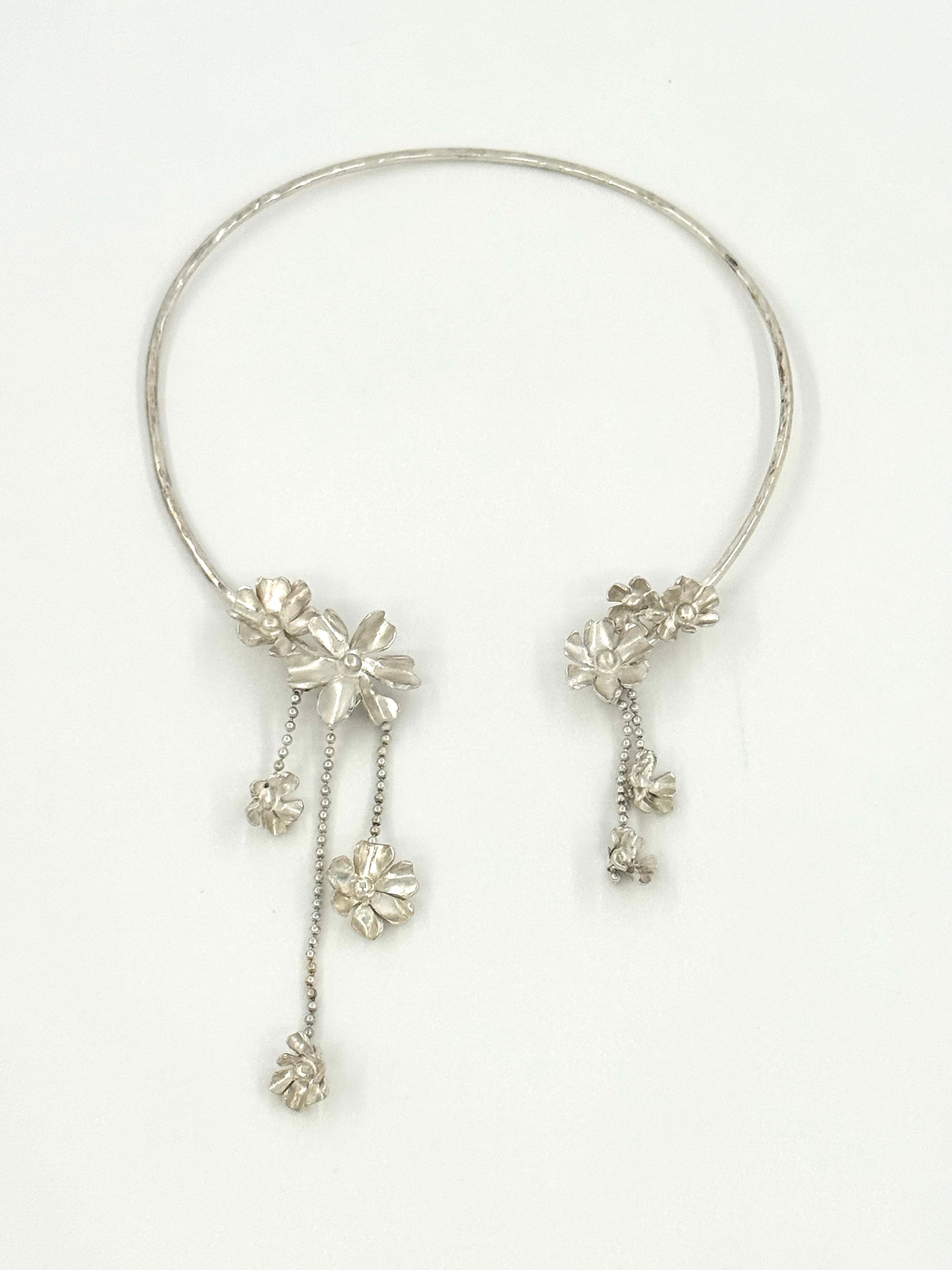 A silver-toned circular collar necklace with dangling floral and chain embellishments, displayed on a clean white background.
