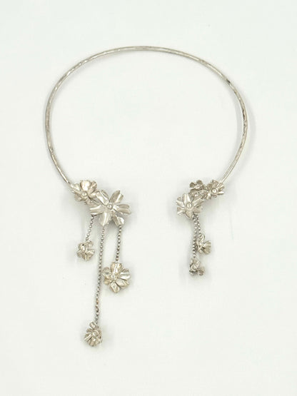 A silver-toned circular collar necklace with dangling floral and chain embellishments, displayed on a clean white background.