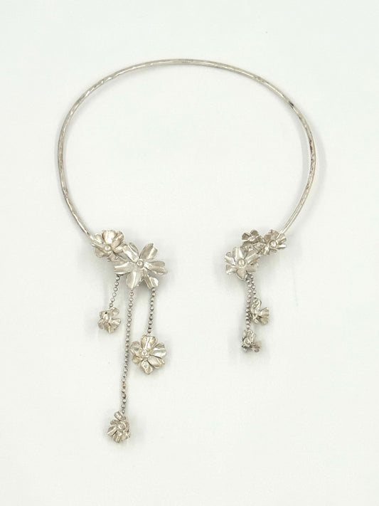 A silver-toned circular collar necklace with dangling floral and chain embellishments, displayed on a clean white background.