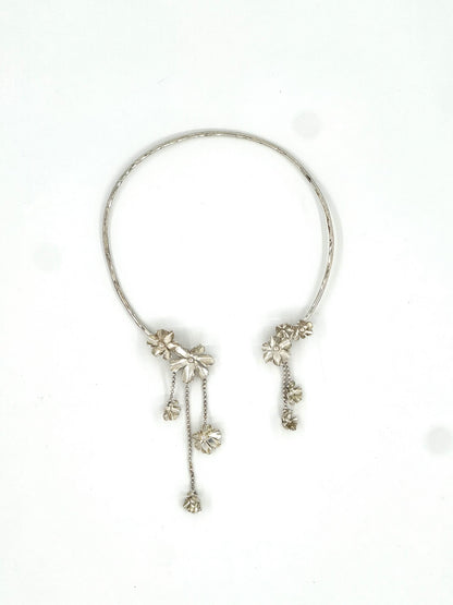 A silver-toned open cuff bracelet with dangling floral and chain embellishments, photographed on a plain white background.